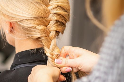Braiding braid. Hands of female hairdresser braids long braid for a blonde woman in a hair salon