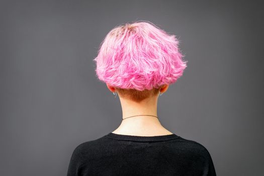Back of female head with curly short pink hair against the dark background