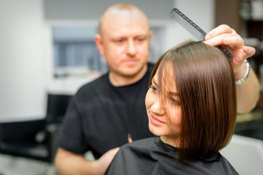 Young caucasian brunette woman having her hairstyling by a male hairdresser at a parlor