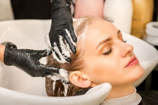 Young caucasian blonde woman having hair washed in the sink at a beauty salon