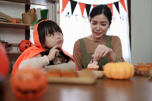 Young girl and mother at Halloween making treats and cupcake on table. Happy Halloween day.