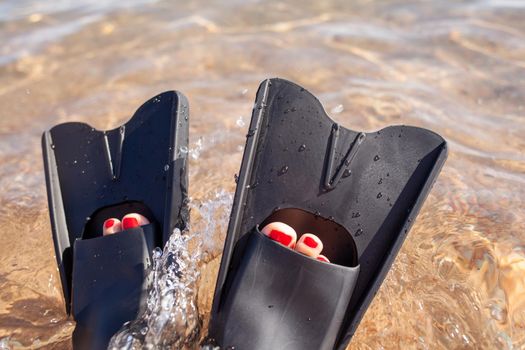 A woman in black flippers splashes near the shore. Fins stick out of the water. Swimming equipment. Summer holidays, fun, exploring the sea world concept. Space for copy.
