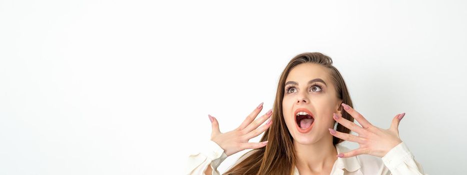 Shocked young caucasian woman with open mouth looking up and expresses surprise isolated over white background. Beautiful surprised brunette woman in studio
