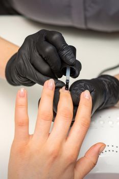 Painting nails of a woman. Hands of Manicurist in black gloves applying transparent nail polish on female Nails in a beauty salon