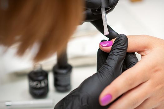 Painting nails of a woman. Hands of Manicurist in black gloves applying pink nail polish on female Nails in a beauty salon