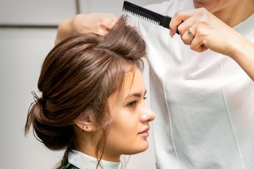 Professional hairdresser doing hairstyle for a beautiful brunette young woman with long hair. Concept of fashion and beauty