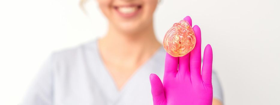 Yellow sugar paste in hand master of depilation. Smiling beautician holding wax for depilation over white background. Concept epilation