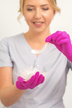 The beautician holds white feathers in her gloved hands over white background. Concept of health softness skin and body care