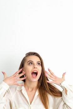 Shocked young caucasian woman with open mouth looking up and expresses surprise isolated over white background. Beautiful surprised brunette woman in studio