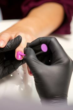 Painting nails of a woman. Hands of Manicurist in black gloves applying pink nail polish on female Nails in a beauty salon