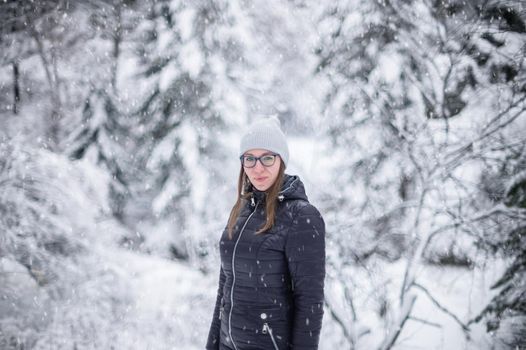 Woman in winter jacket walking in snowy winter forest, snowy winter day