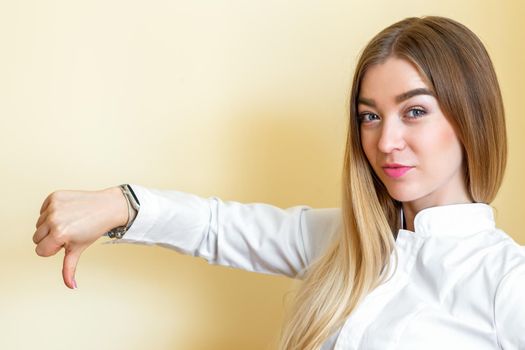 A woman showing dislike. Young beautiful businesswoman wearing a white shirt with thumb down isolated over a yellow background