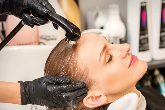 Young caucasian blonde woman having hair washed in the sink at a beauty salon