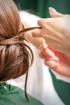 Professional hairdresser doing hairstyle for a beautiful brunette young woman with long hair. Concept of fashion and beauty