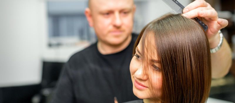 Young caucasian brunette woman having her hairstyling by a male hairdresser at a parlor