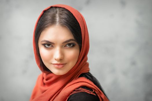 Portrait of a pretty young caucasian woman with makeup in a red headscarf on gray background