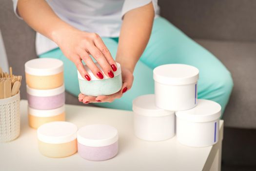 Female hands open a white body cream jar over the table with many jars of cosmetics