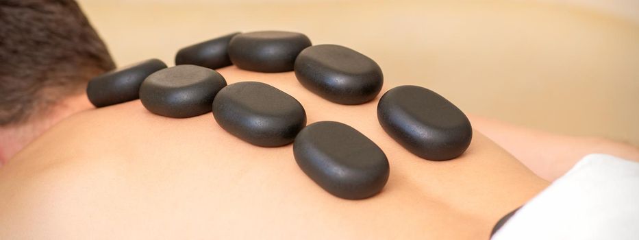 Hot stone massage therapy. Caucasian young man getting a hot stone massage on back at spa salon