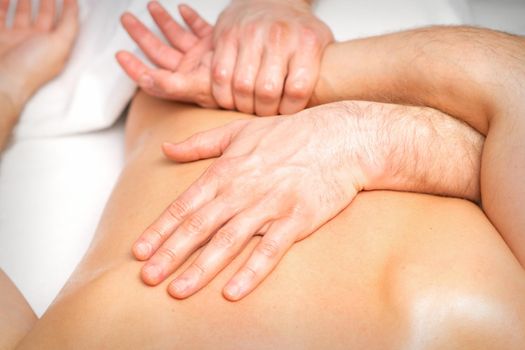 A male physiotherapist stretches the arms on the back of a man lying down, close up