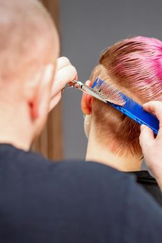 Woman having a new haircut. Male hairstylist cutting pink short hair with scissors in a hair salon