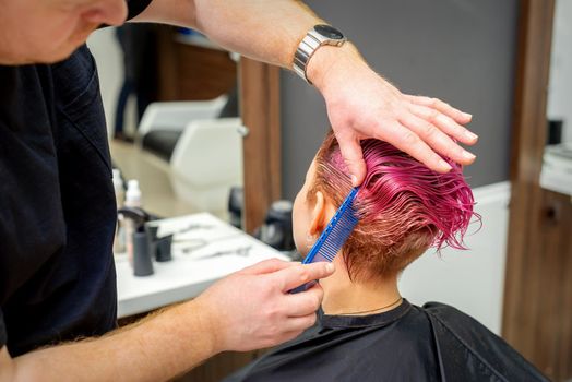 Hands of hairdresser combing hair making short pink hairstyle for a young caucasian woman in a beauty salon