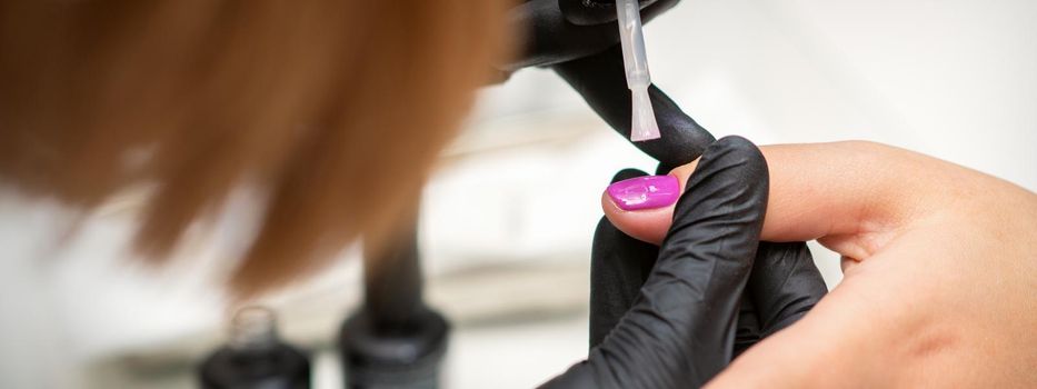 Painting nails of a woman. Hands of Manicurist in black gloves applying pink nail polish on female Nails in a beauty salon