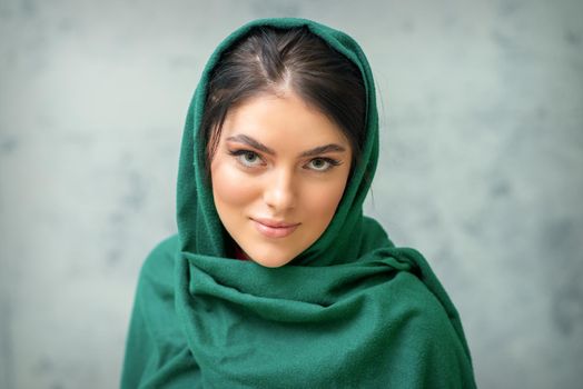 Portrait of a pretty young caucasian woman with makeup in a green headscarf on gray background