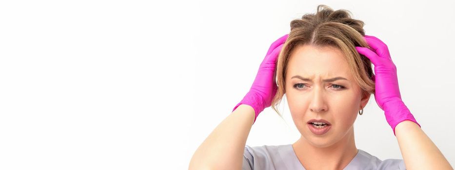 The emotionally shocked young female medical worker holding hands on her head fell into panic on white background, infection, epidemic, virus, and disease concept