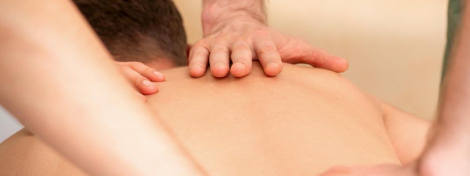 Young man receiving back massage in four hands in spa beauty salon