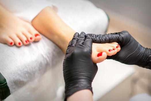 Foot massage with moisturizing and peeling cream by pedicurist hands wearing black gloves, close up