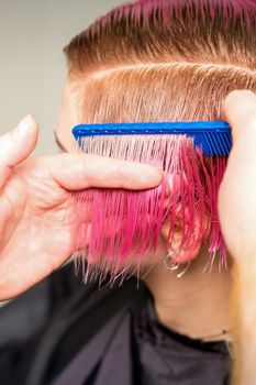 Hands of hairdresser combing hair making short pink hairstyle for a young caucasian woman in a beauty salon