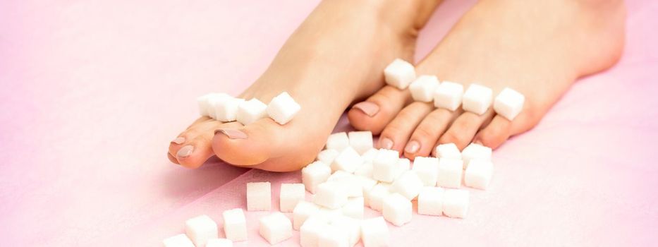 Sugar cubes lying in a row on female feet on pink background with copy space, depilation concept