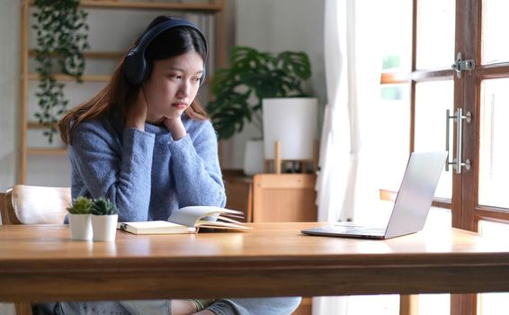 Side View Of Asian Businesswoman Using Computer Working Online And Browsing Internet Wearing Wireless Earphones Sitting In Modern Office Indoor. Business Career, Internet And Technology.