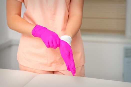 Hand of beautician puts on sterile pink gloves prepares to receive clients indoors