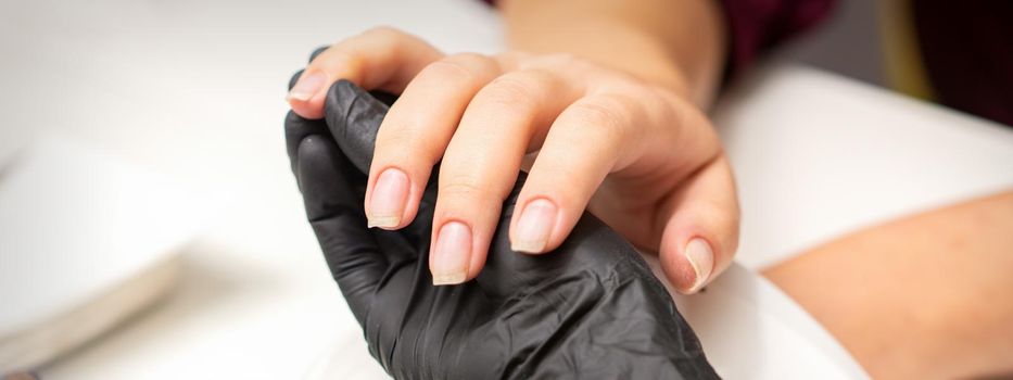 Examination of manicured fingernails. Hands of manicure master in black gloves examining female transparent nails in manicure salon