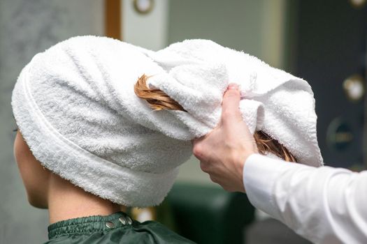 A hairdresser is wrapping the wet hair of the young woman in a towel after washing at the beauty salon