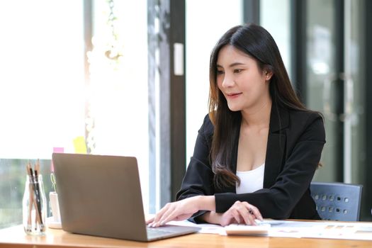 Young Asian businesswoman using a calculator to calculate business principles. Accounting statistics concept at the office..