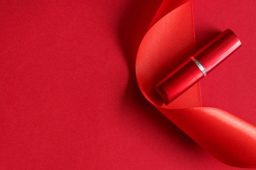 Cosmetic branding, glamour lip gloss and shopping sale concept - Luxury lipstick and silk ribbon on red holiday background, make-up and cosmetics flatlay for beauty brand product design