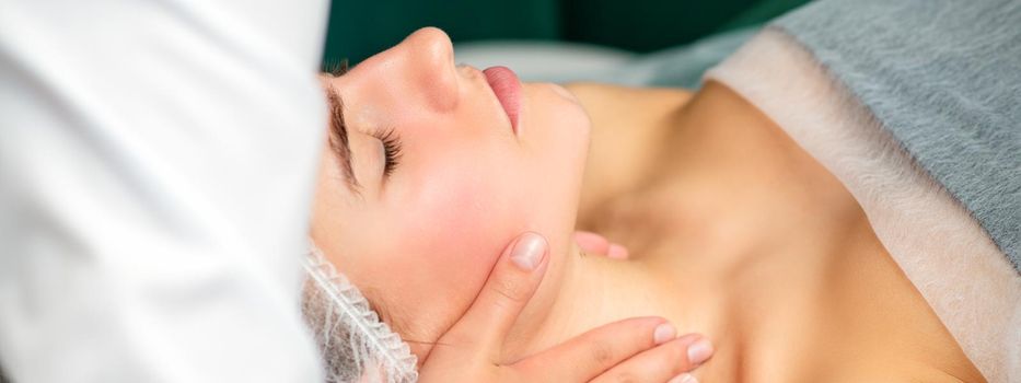 Massaging female neck. Young caucasian woman receiving neck massage relaxing in spa salon