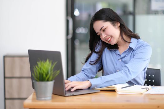 Beautiful young Asian businesswoman charming smiling and talking on the mobile phone in the office..