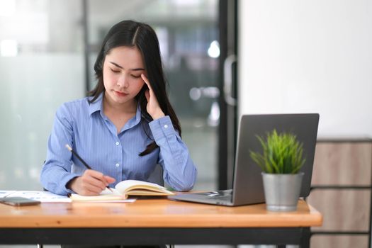Stressful day. Young Asian businesswoman stressed while working on laptop at office..