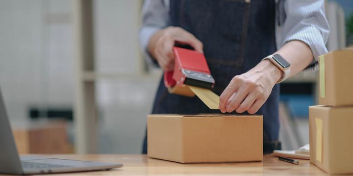 Close up online business owner prepares product for delivery to the customer. Online entrepreneur using scotch tape to seal parcel box. small business owner, SME concept..
