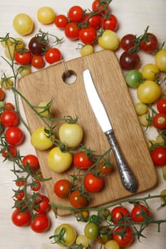 Little red, yellow, green and black cherry tomatoes on white table with wooden cutting board in the middle as a place for text, copy space, nature background, flat lay, top view.