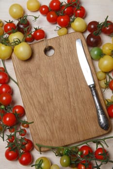 Little red, yellow, green and black cherry tomatoes on white table with wooden cutting board in the middle as a place for text, copy space, nature background, flat lay, top view.