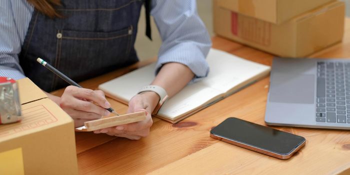 Shipping shopping online ,young start up small business owner writing address on cardboard box at workplace.small business entrepreneur SME or freelance asian woman working with box at home.