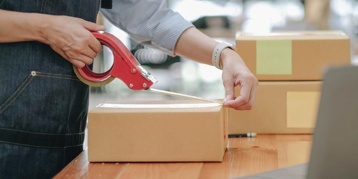 Small business entrepreneur SME, asian young woman,girl owner packing product, checking parcel for delivery to customer, using scotch tape to seal the box, working at home. Merchant online, e commerce.