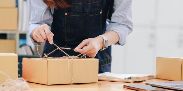 Starting small business, SME owner, female entrepreneurs are using the rope to tie boxes to pack products Order online to prepare to pack a box of goods for sale to customers, sme business idea online.