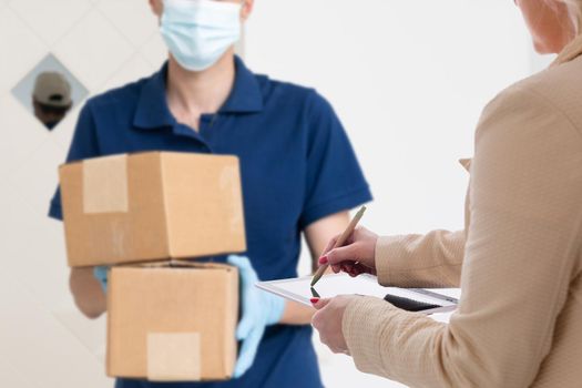 delivery, mail, people and shipping concept. Young woman sign in tablet after receiving parcel from courier at home