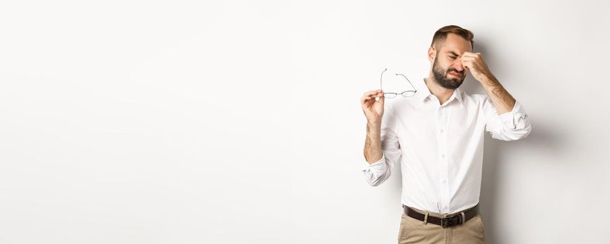 Tired businessman take-off glasses and rubbing eyes, standing exhausted against white background.