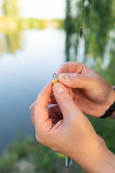 The concept of bait for fish. Close-up of a fisherman's male hand stringing bait on a fishing rod against a blue lake